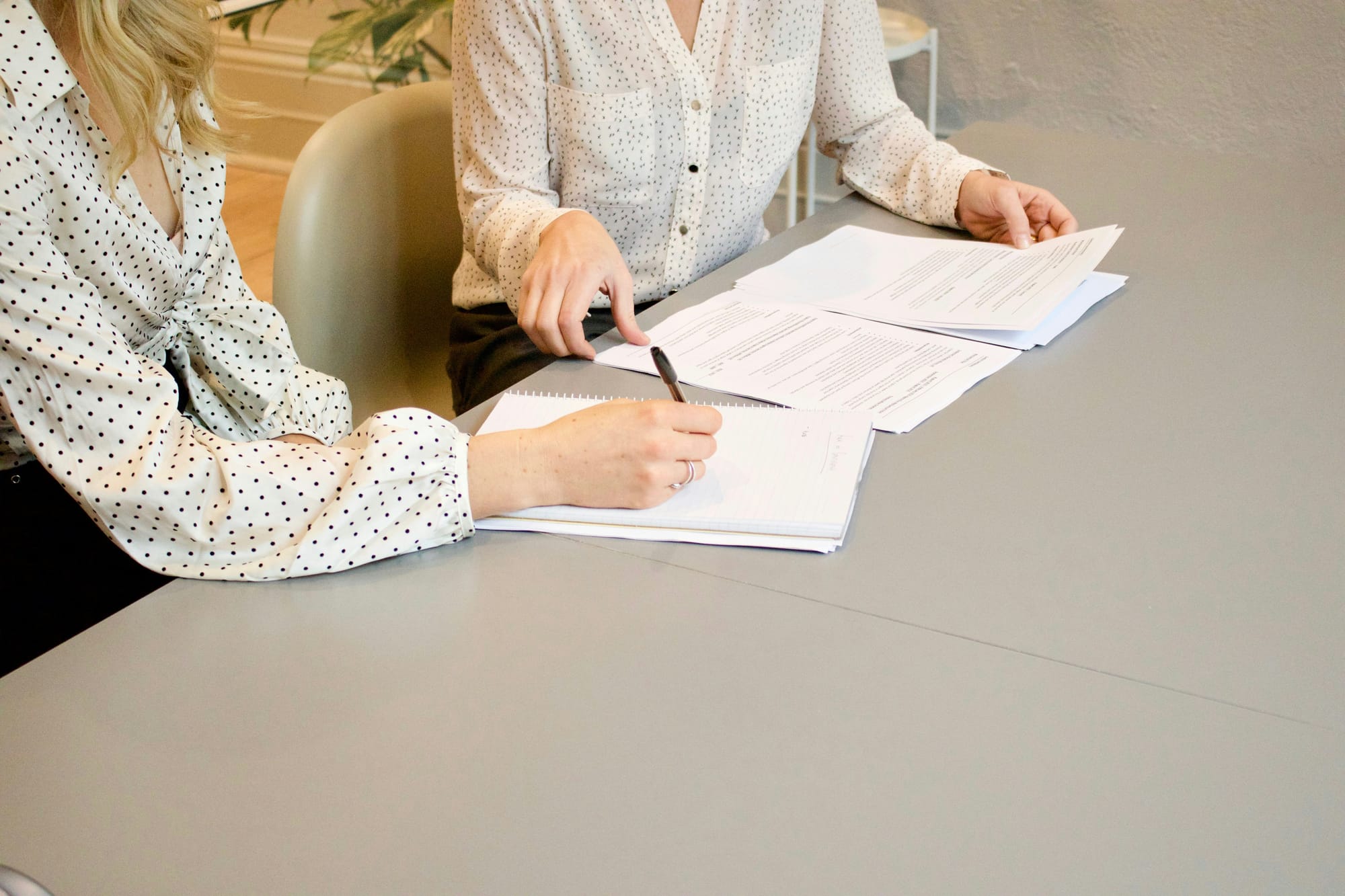 Two persons signing paper documents on a gray table